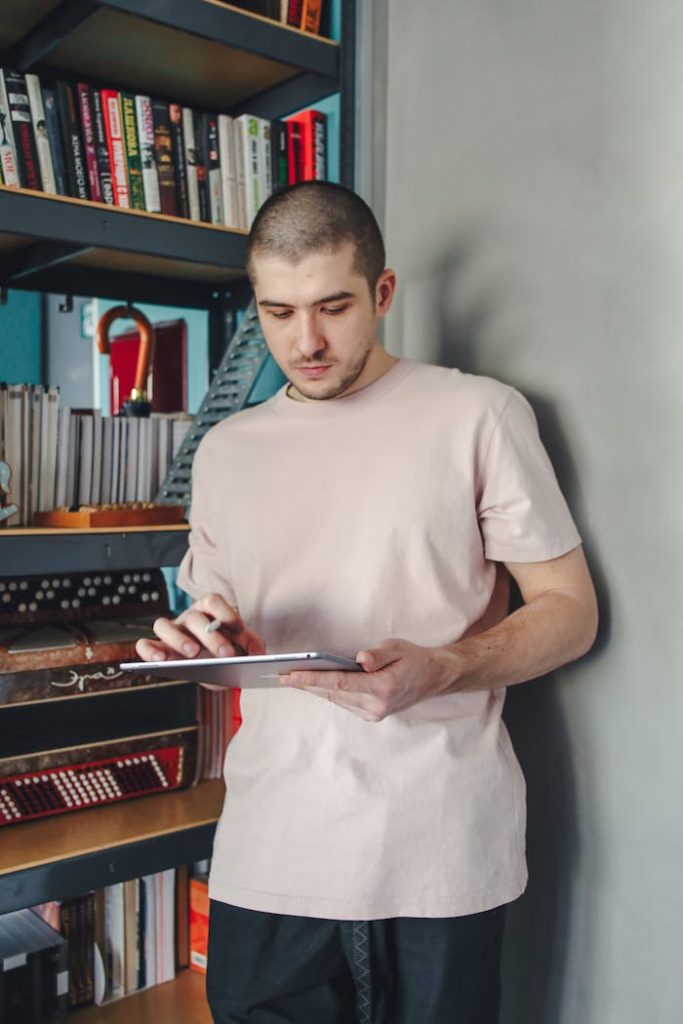 Man using a digital tablet while standing in a home library filled with bookshelves.