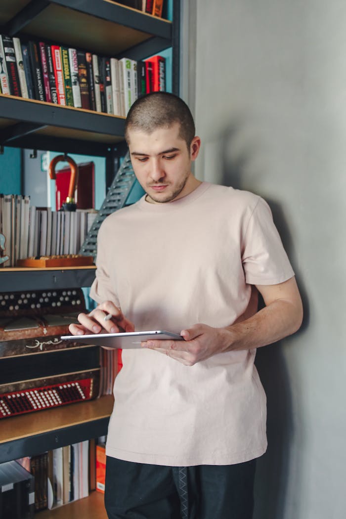 Man using a digital tablet while standing in a home library filled with bookshelves.