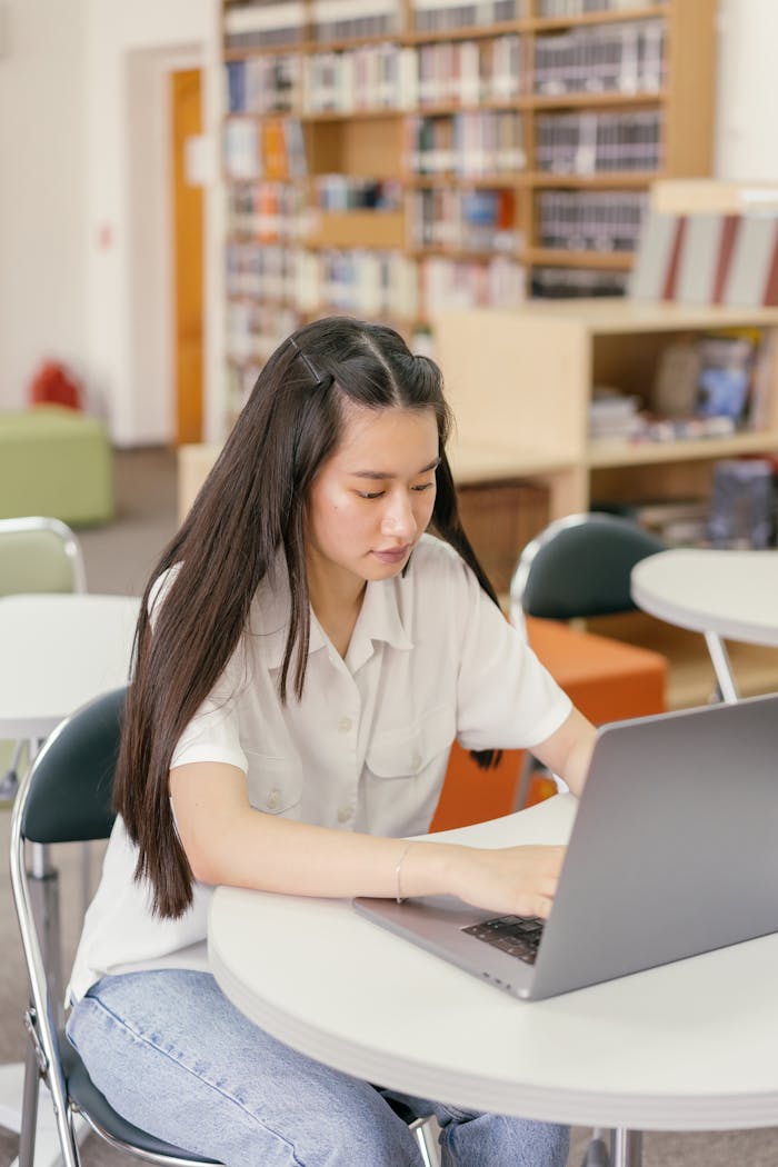 Focused young woman working on a laptop in a library setting.
